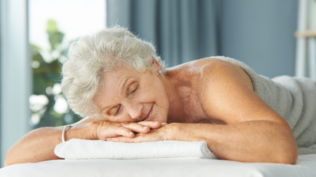 Une femme agée est allongée sur une table de massage, sur le ventre pour un massage bien-être intégral du corps  