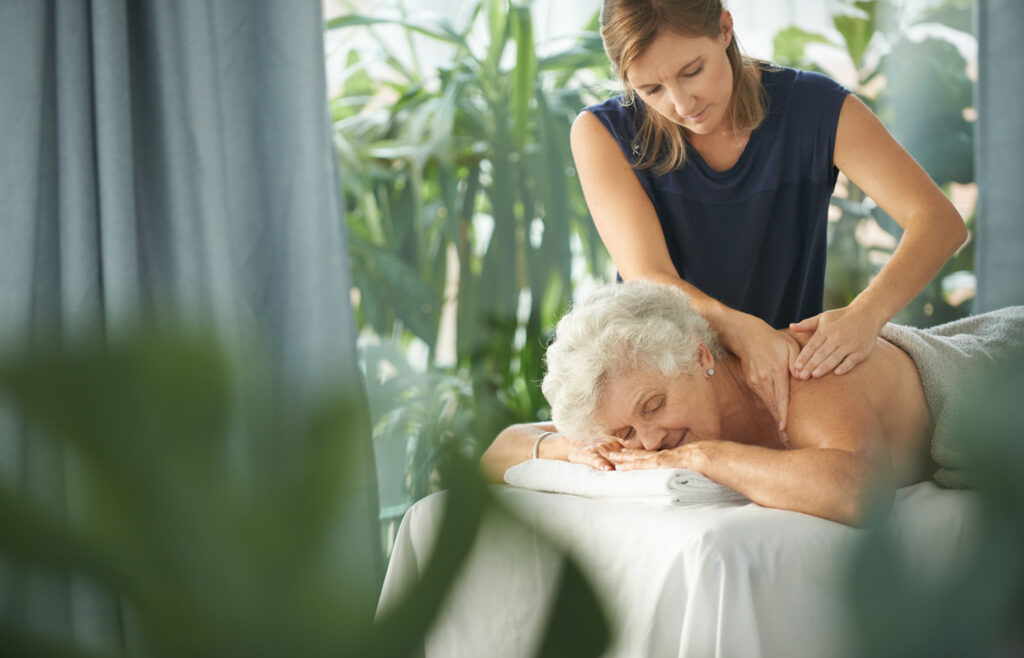 Une masseuse professionnelle réalise un massage doux et relaxant du dos sur une femme sénior allongée sur le ventre 